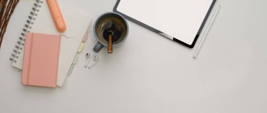 Tablet, kırtasiye malzemesi, kahve fincanı ve beyaz masadaki fotokopi alanı ile çalışma masasının üst görünümü 