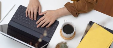 Tablet klavyesinde kahve fincanı, kitap ve kaktüs tenceresiyle yazı yazan bir kadın resmi.