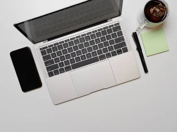 Top view of portable workspace with computer laptop, smartphone, pen, notepad and coffee mug on white desk