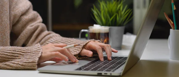 Ofis masasında dizüstü bilgisayarda bir bardak içecek ve dekorasyonla yazı yazan bir kadının yan görüntüsü