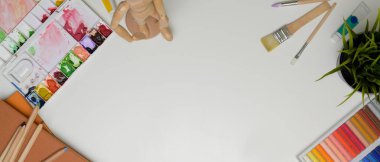 Boya araçları, defter, dekorasyonlar ve beyaz masadaki boşluğu kopyalayan çalışma alanının üst görünümü