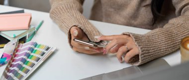 Çalışma yerinde ofis malzemeleriyle otururken akıllı telefon kullanan kadın ellerini kapat