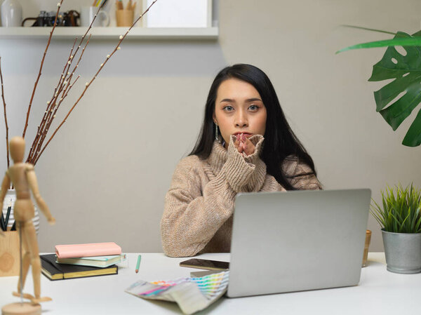 Portrait of female office worker sitting at office desk with supplies, stationery and decorations in office room 