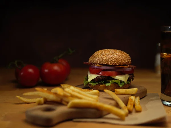 Close up view of French fries, fresh tasty burger, ingredients and beverage on rustic wooden table