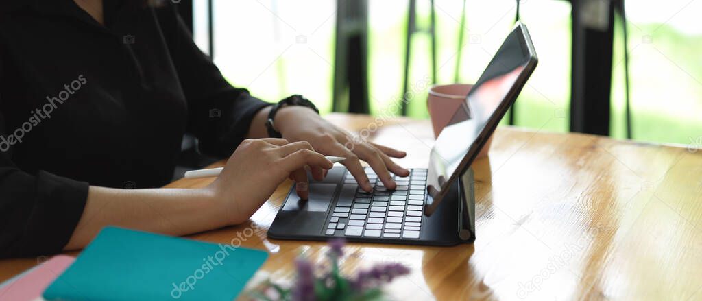 Side view of female hands typing on tablet keyboard on worktable in glass wall office room  