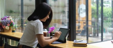 Kafedeki ahşap barda dijital masa ile ödev yapan bayan üniversite öğrencisinin yan görüntüsü. 