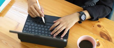 Dişi ellerin dijital tablet kullanırken çekilen resmi. Stylus ve klavye tahta masa üzerinde. 