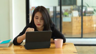 Kütüphanedeki masada dijital tablet ve kitaplarla işine konsantre olan bir kadının portresi 