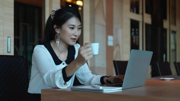 Portrait of female entrepreneur holding coffee cup while working with laptop and supplies on meeting table