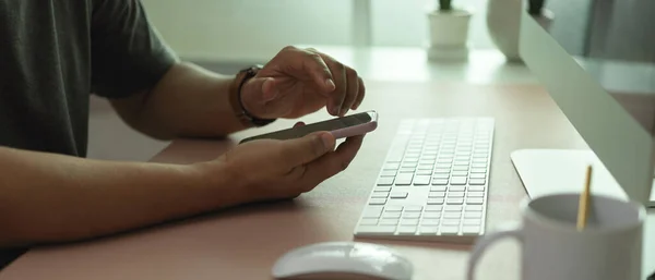 Side view of male office worker using smartphone on office desk with computer and office supplies