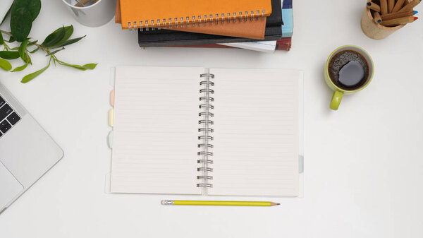 Top view of study table with opened blank notebook, laptop, stack of books, pencils and coffee cup