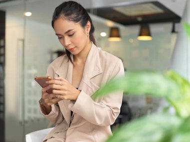 Cam bölme ofisinde otururken akıllı telefon kullanan kadın girişimcinin portresi