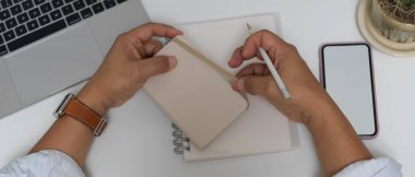 Ofis masasında ofis malzemeleriyle çalışırken erkek girişimcinin ajandanın açılışını gösteren bir fotoğraf. 