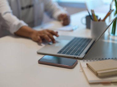 Çalışma odasındaki not defterine not alırken erkek elinin dizüstü bilgisayar kullanırken görüntüsü kesilmiş. 