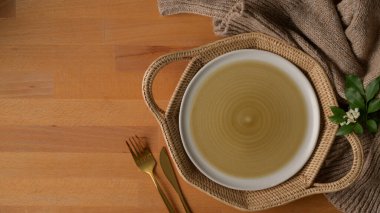 Hasır tepsi, gümüş çatal bıçak, fotokopi alanı, masa örtüsü ve dekorasyonla ahşap mutfak masasının üst görüntüsü. 