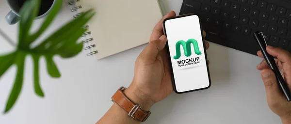 Overhead shot of male hand using mock up smartphone screen while working on office desk