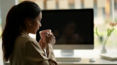 Kadın ofis çalışanının portresi ofis odasındaki bilgisayar masasında rahatça oturup kahve içiyordu. 
