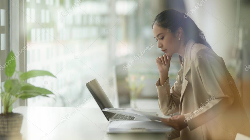 View through glass window of female entrepreneur concentrating on her work on office desk