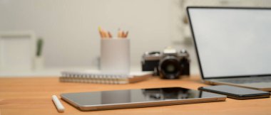 Çalışma alanını dijital tablet, laptop, kamera, akıllı telefon ve ahşap masadaki kırtasiye ile kapat