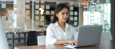 Cam bölme odasındaki toplantı masasında dizüstü bilgisayarla çalışan kadın ofis çalışanının portresi. 