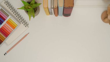 Fotokopi alanı, kitapları, saksısı, kırtasiyesi ve yağlı pastelleri olan çalışma masasının üst görünümü 