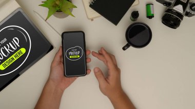 Erkek ellerinin çalışma masasında tablet, kamera ve malzemelerle sahte akıllı telefon kullanarak yukarıdan çekimleri. 