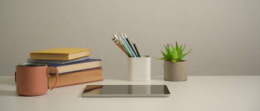 Çalışma masasını dijital tablet, kitap, kırtasiye, kupa ve dekorasyonla kapatın 