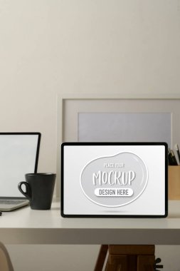 Tablet, laptop, kupa, kırtasiye malzemesi ve çalışma odasındaki çerçeve ile eklenmiş çalışma tablosu 