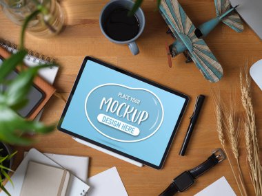 Çalışma alanının en üst görünümü dijital tablet, aksesuarlar, kırtasiye malzemeleri ve ahşap masa süslemeleri ile 
