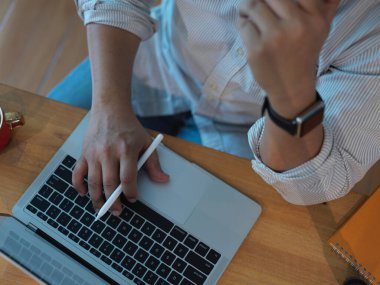 Modern ofis odasındaki ahşap masa üzerinde dizüstü bilgisayarla çalışan erkek ofis çalışanının en üst görüntüsü.