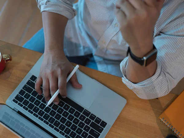 Modern ofis odasındaki ahşap masa üzerinde dizüstü bilgisayarla çalışan erkek ofis çalışanının en üst görüntüsü.
