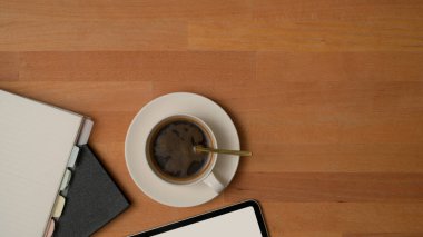 Üzerinde bir fincan kahve, defter, tablet maketi ve ahşap masa üzerindeki boşluğu kopyalayarak işe yarar bir görünüm.