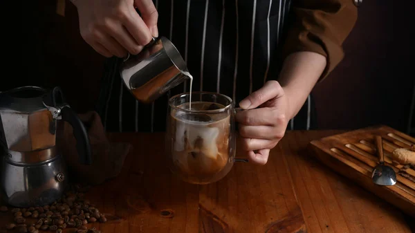 Close up view of barista pouring milk into a cup of coffee on wooden counter bar in coffee shop