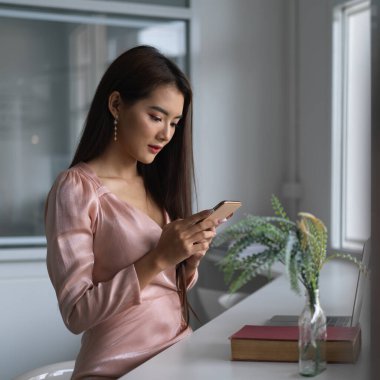 Ofisteki akıllı telefonuna bakarken akıllı telefonu tutan genç bir iş kadını. 