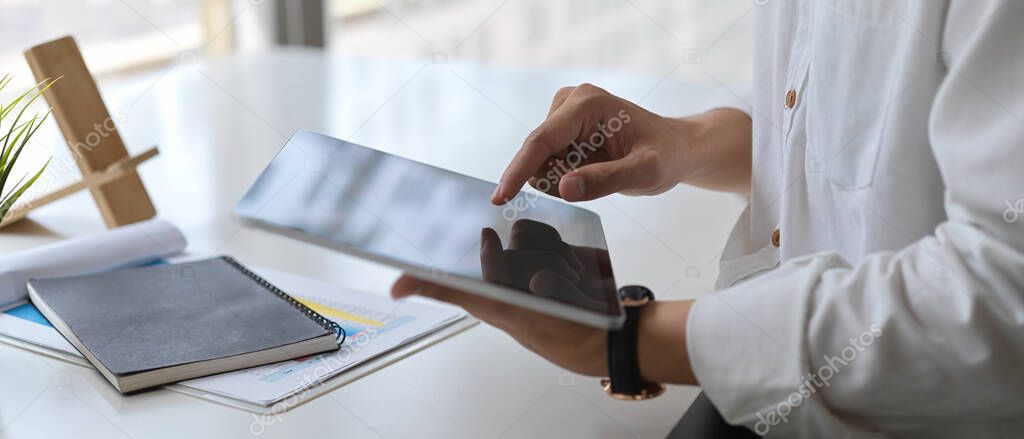 Close-up view of young businessman working on his company plan while using tablet in office room 