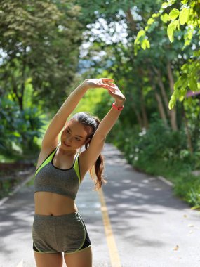 Genç formda Asyalı bayan sporcu parkta egzersiz yapmadan önce kollarını açıyor. 