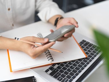 Ofis odasında çalışırken elinde akıllı telefon olan genç işadamının yakın plan görüntüsü. 
