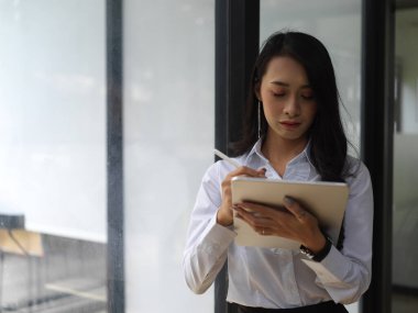 Cam duvar toplantı odasında dikilirken dijital tablet kullanan kadın işçinin portresi 