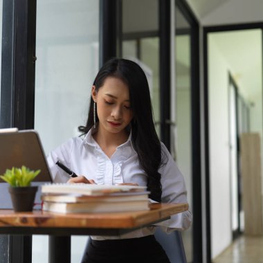 Ofis odasındaki kitaplara, laptoplara ve malzemelere odaklanan bir kadının portresi. 