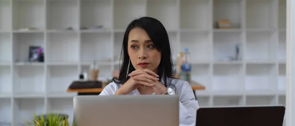 Portrait of female office worker thinking about her work while sitting in office room