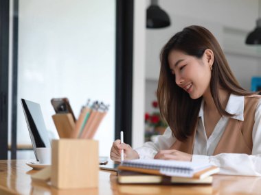 Kafedeki masada dijital cihazlar ve kırtasiyeyle ödev yapan gülümseyen üniversite öğrencisi portresi 