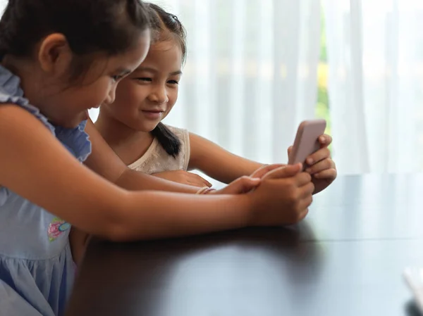 居間のテーブルの上で一緒にスマートフォンで遊んでいる2人の女の子の側面図 — ストック写真