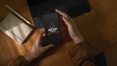 Klavye ve günlük kitabıyla ahşap masada akıllı telefon kullanan bir kadının yukarıdan çekilmiş fotoğrafı.