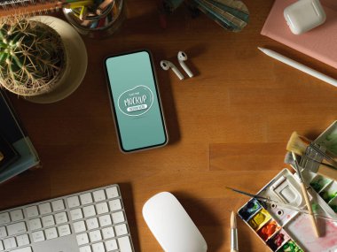 Akıllı telefon, klavye, boya aletleri ve malzemelerle ahşap masa üst görünümü 