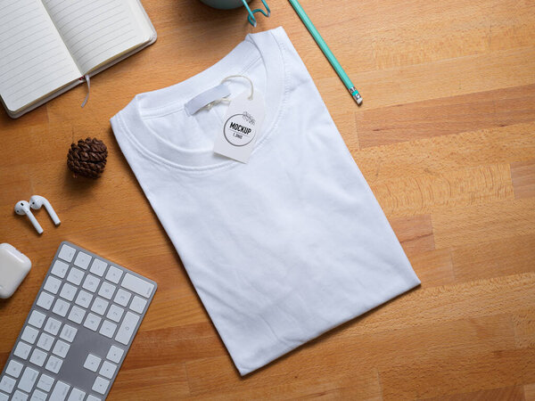 Top view of mock up white t-shirt with price tag on wooden worktable with supplies 