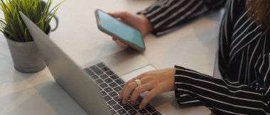 Çalışan bilgisayardaki akıllı telefon ve dizüstü bilgisayarla çalışan bir kadının görüntüsü. 