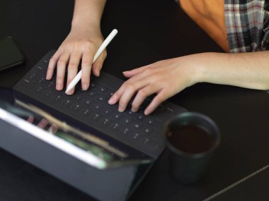 Tablet klavyesinde kahve fincanı ile siyah masada yazan kadın ellerinin üst görüntüsü