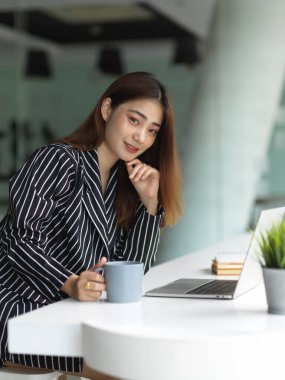 Ofiste kahve molası verirken kameraya bakan kadın ofis çalışanının portresi. 