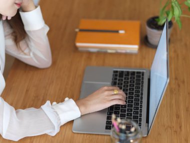 Tahta ofis masasında dizüstü bilgisayarla çalışan kadın elinin yan görüntüsü. 