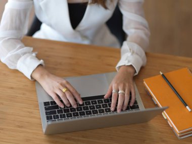 Kırpılmış kadın eli, kırtasiyeli ahşap masadaki dizüstü bilgisayarın klavyesinde daktilo kullanıyordu.